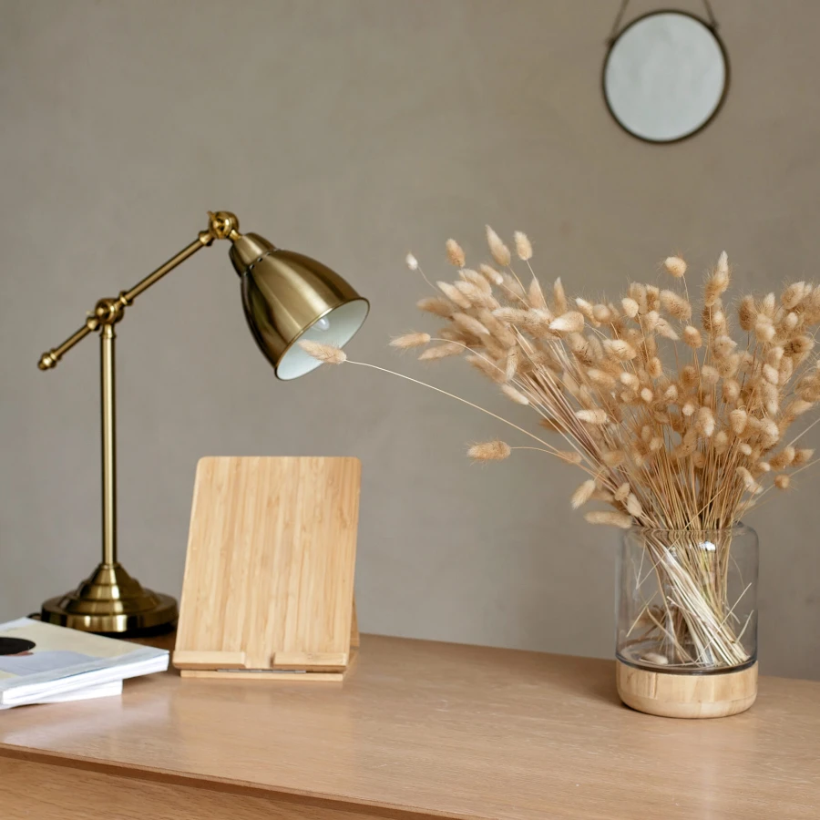 Natural wooden table in a modern style in beige tones with a vase of dried flowers and a copper lamp. Home Office. Interior Design.
